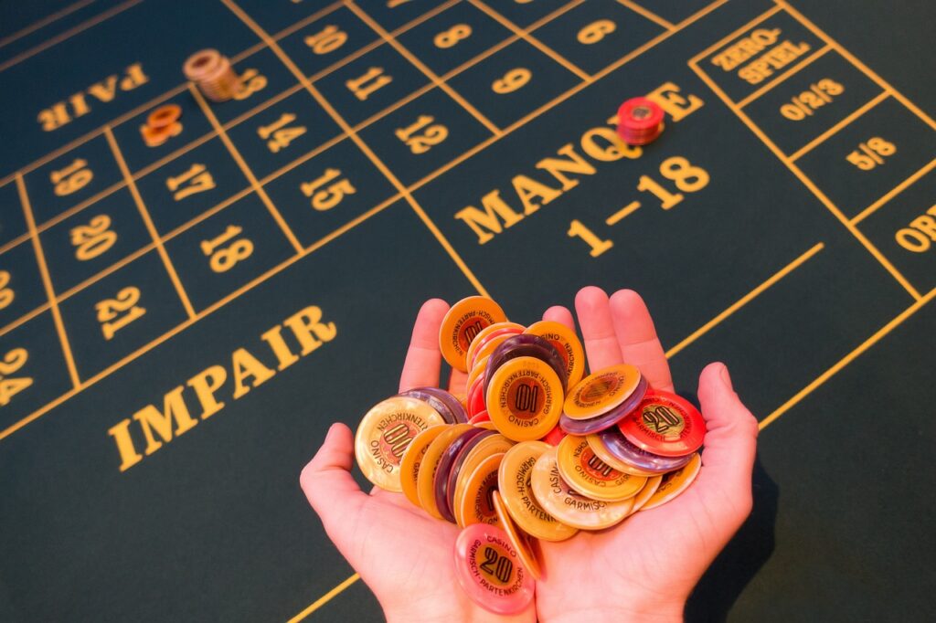 Two hands holding casino chips over a Roulette table